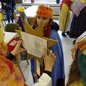 Drei als Sternsinger verkleidete Kinder bekleben die hintere Seite ihres Sterns mit dem Liedblatt